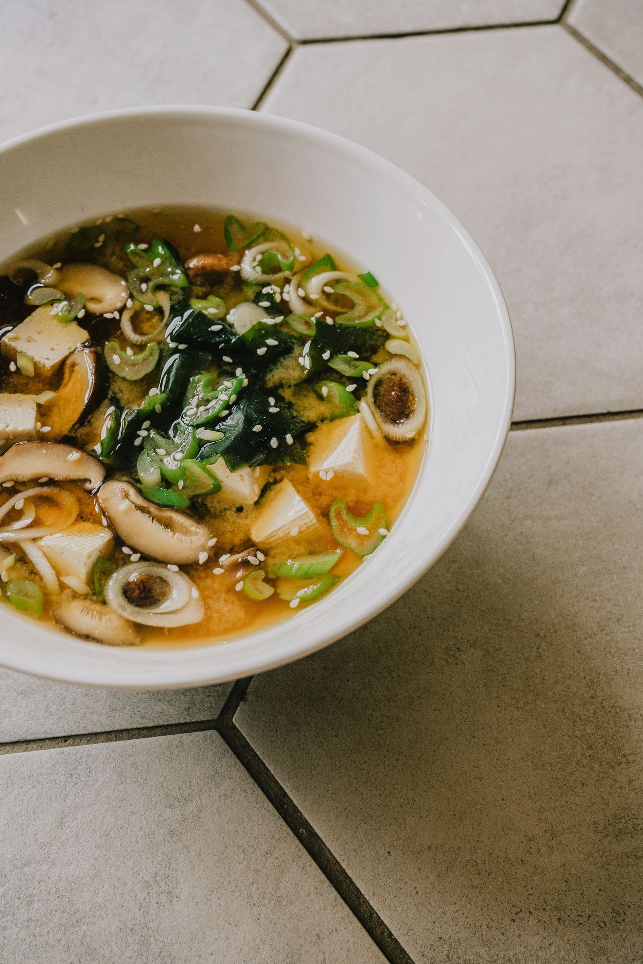 a white bowl filled with soup on top of a tiled floor