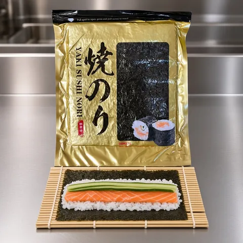 Sheet of nori with rice, salmon and cucumber on a bamboo rolling mat in front of a Yaki Sushi Nori bag