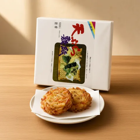 Kakiage vegetable and shrimp fritters on white tempura paper in front of a QING tempura paper pack