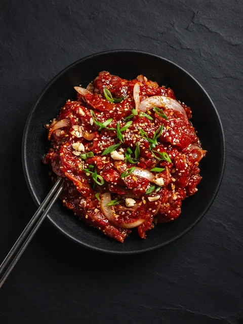 Sliced beef marinated in spicy red bulgogi sauce with onion and sesame in a black bowl