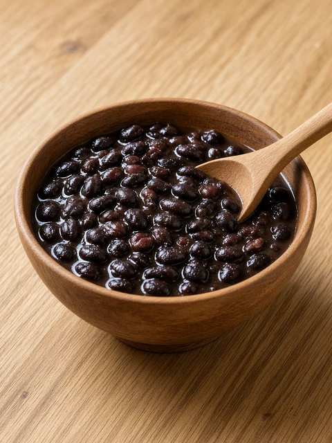 Wooden bowl of glossy black beans with a spoon
